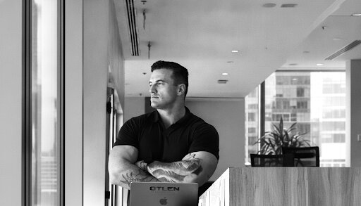 James Richman standing with arms crossed beside a laptop marked OTLEN.